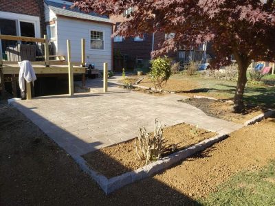 stone patio wrapping around a house and unfinished porch with flowerbeds incorporated into the pattern
