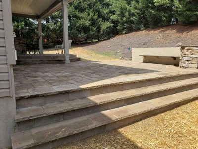 new stone patio next to a covered patio with stone steps between the two patios and steps between the patio and grass