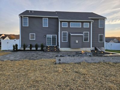 large new patio after brand new patio spanning the width of the house with a firepit and steps up to a back door