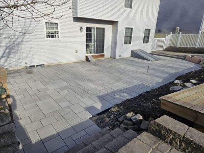 backyard patio spanning the width of a house connecting the back door and basement door as well as leading towards the back of the yard, dogs in the doorway